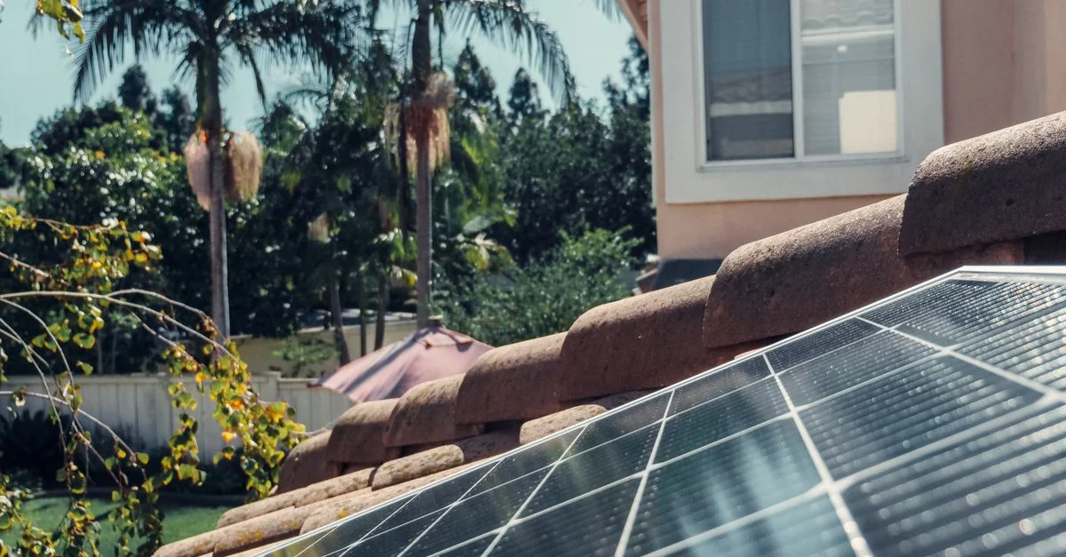 Plan rapproché de panneaux solaires sur un toit avec des palmiers et une maison en arrière-plan.