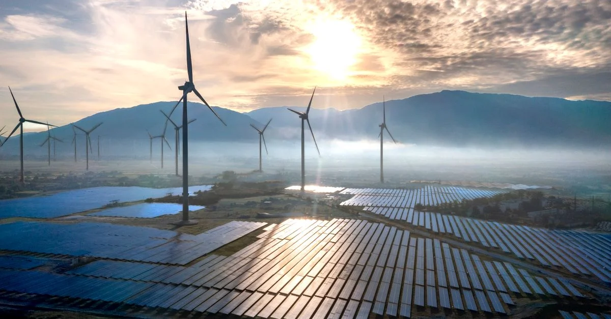 Superbe vue aérienne d'éoliennes et de panneaux solaires au lever du soleil, avec des montagnes et de la brume en arrière-plan.